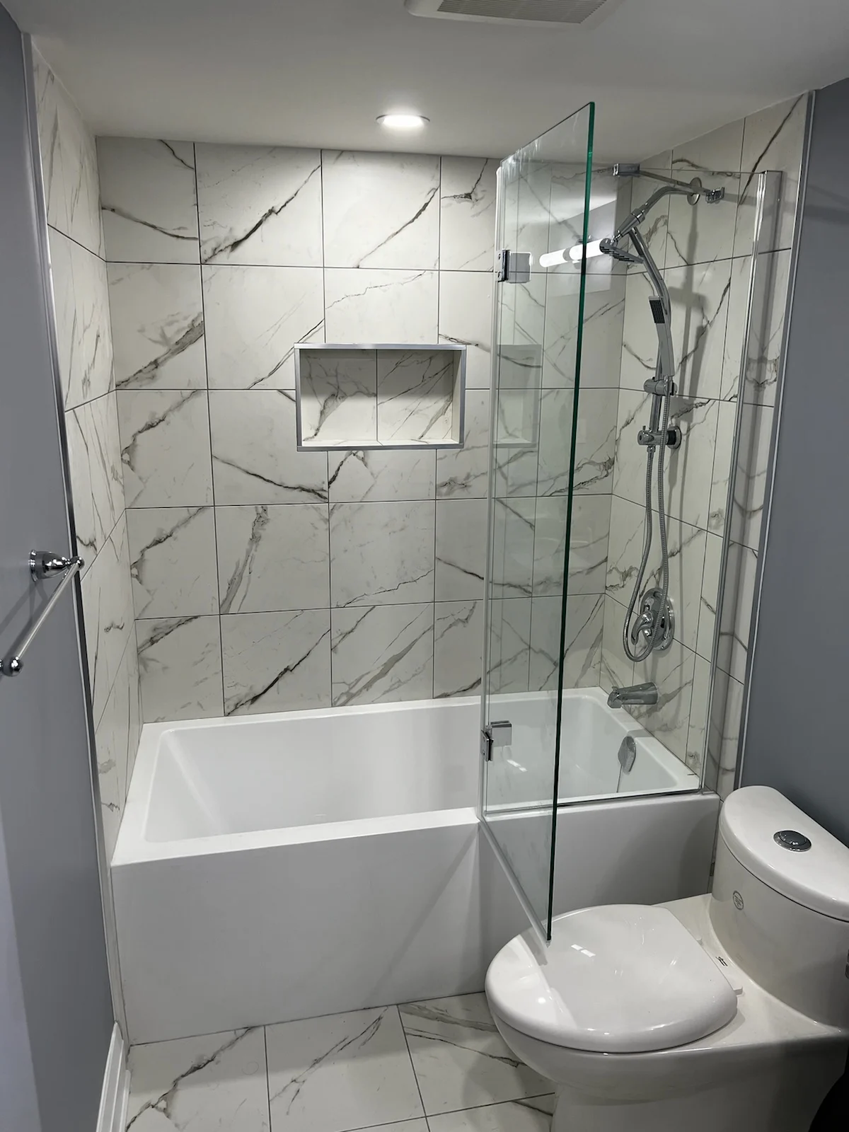 Bathroom renovation featuring a marble-tiled shower with a bathtub and modern fixture